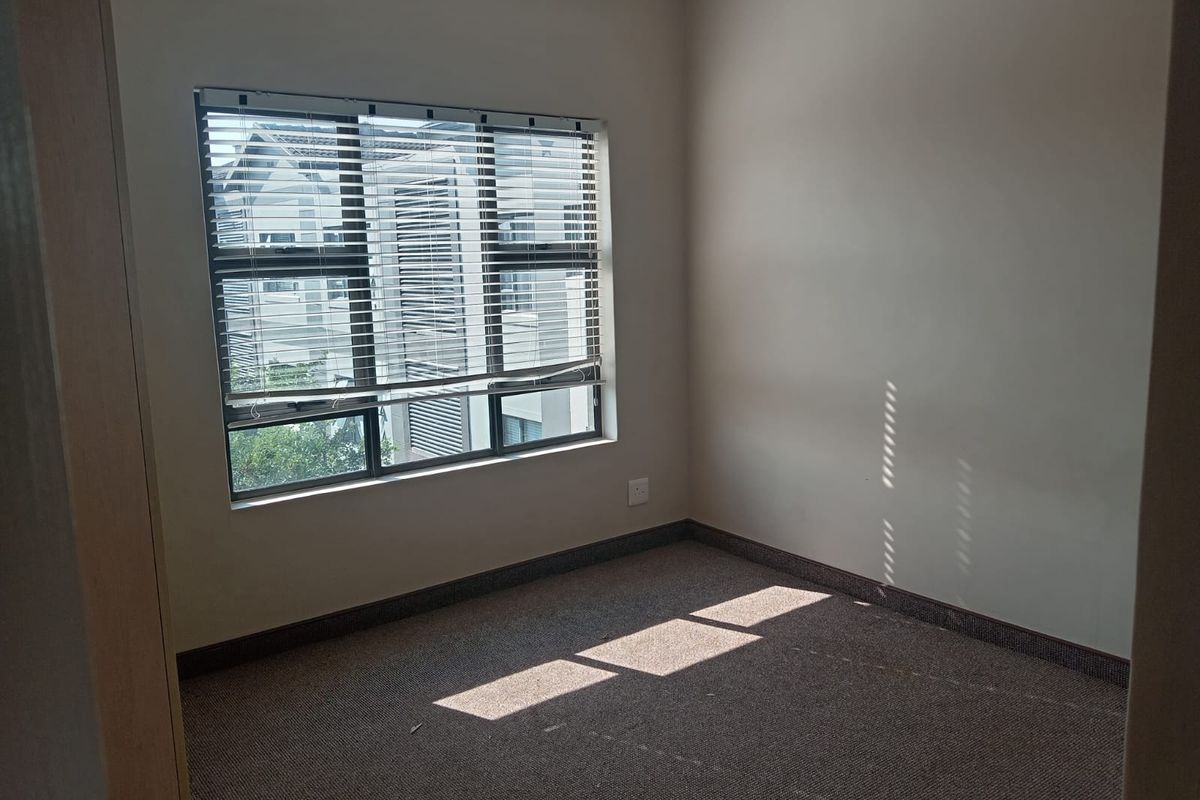 A vacant bedroom featuring neutral wall tones, carpeted flooring, and a window fitted with horizontal blinds.