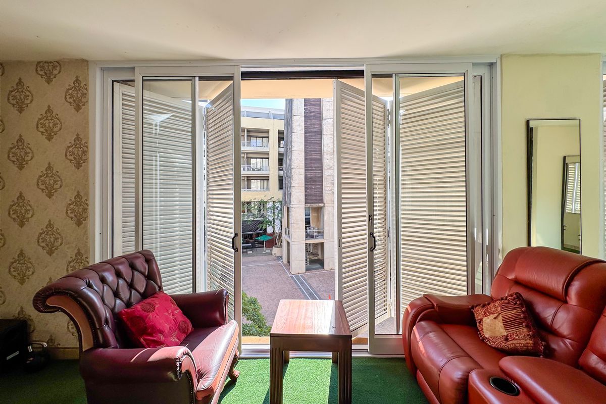 A view from an interior space through large sliding glass doors with integrated security shutters, looking out onto a paved courtyard area.