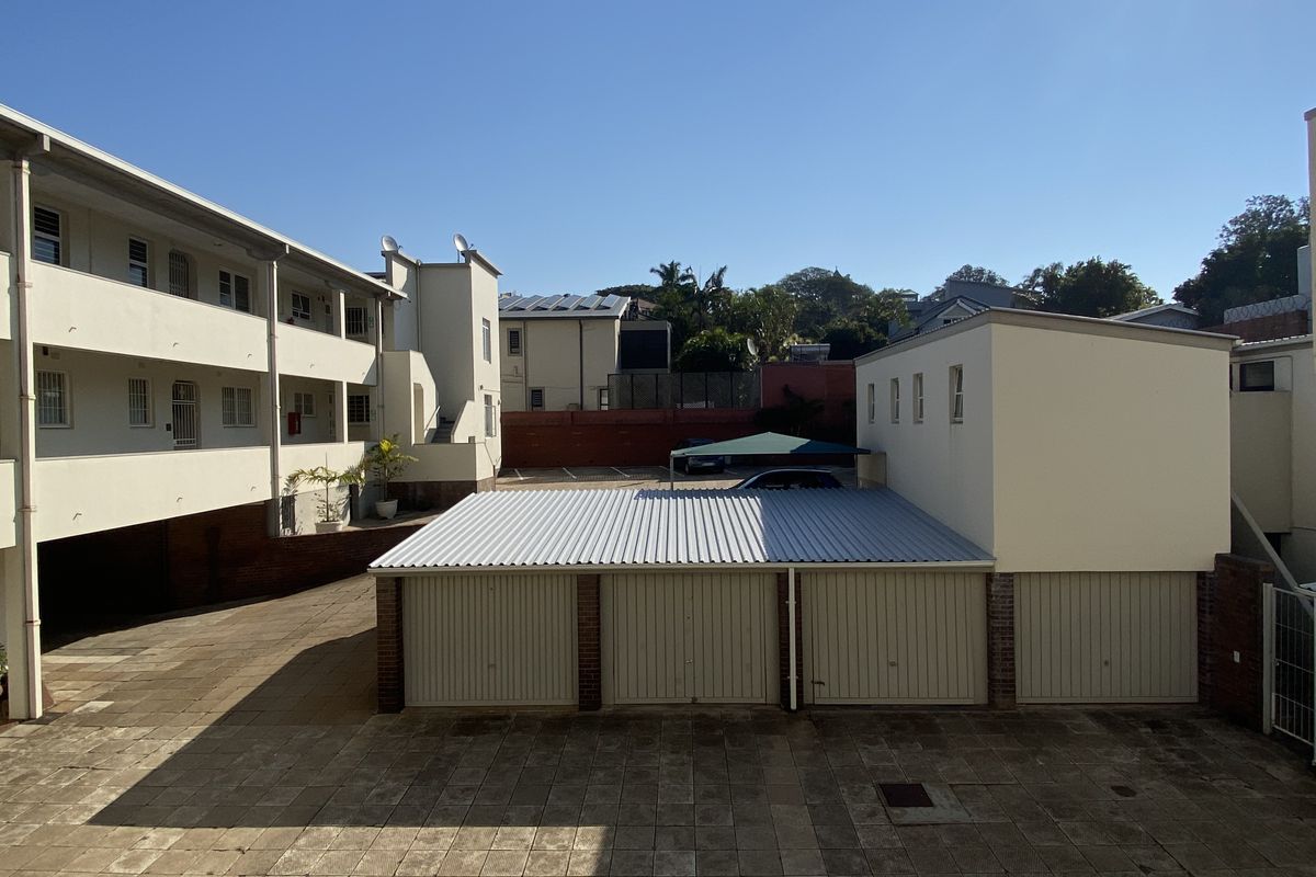 Exterior view of the apartment complex courtyard featuring a row of lock-up garages and paved communal parking area.