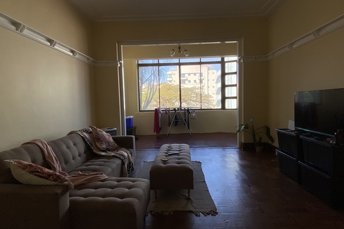 Spacious living area featuring original timber flooring, decorative wall molding, and large windows providing natural light and an urban outlook.