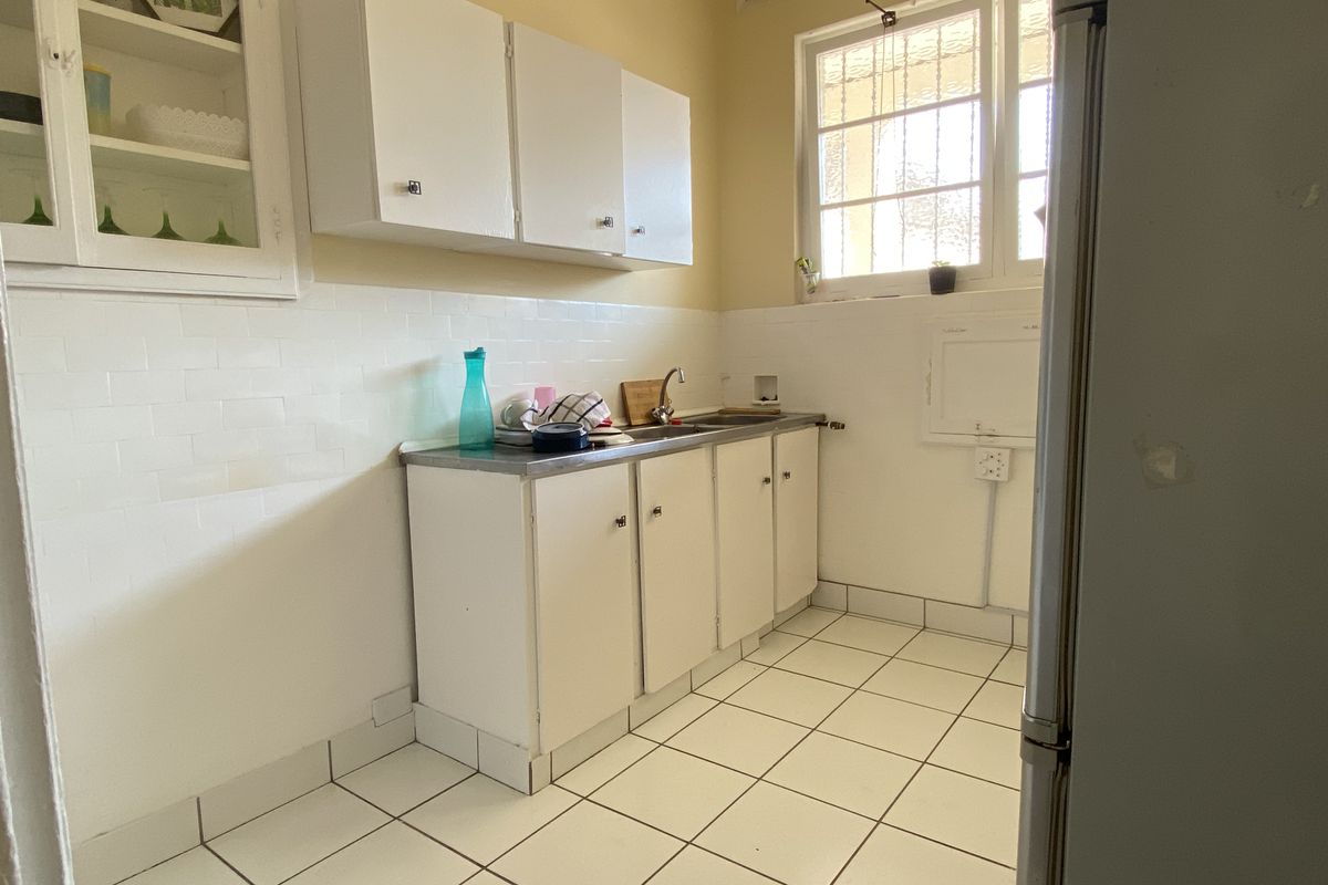 A compact kitchen featuring white cabinetry, a stainless steel sink, subway tile backsplash, and tiled flooring with a window for natural light.
