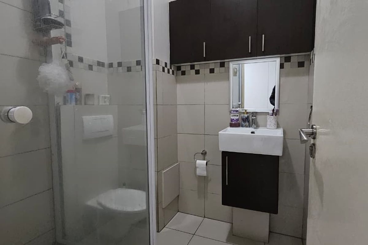 A compact bathroom featuring a wall-mounted vanity, a shower enclosure with a glass door, and a concealed cistern toilet.