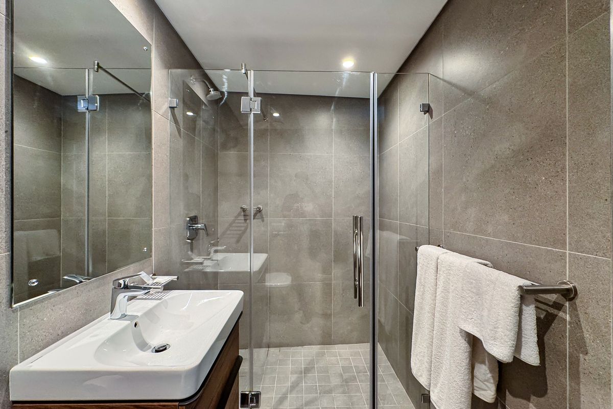 Modern bathroom featuring a glass-enclosed walk-in shower, wall-mounted vanity with basin, large mirror, and neutral floor-to-ceiling tiling.
