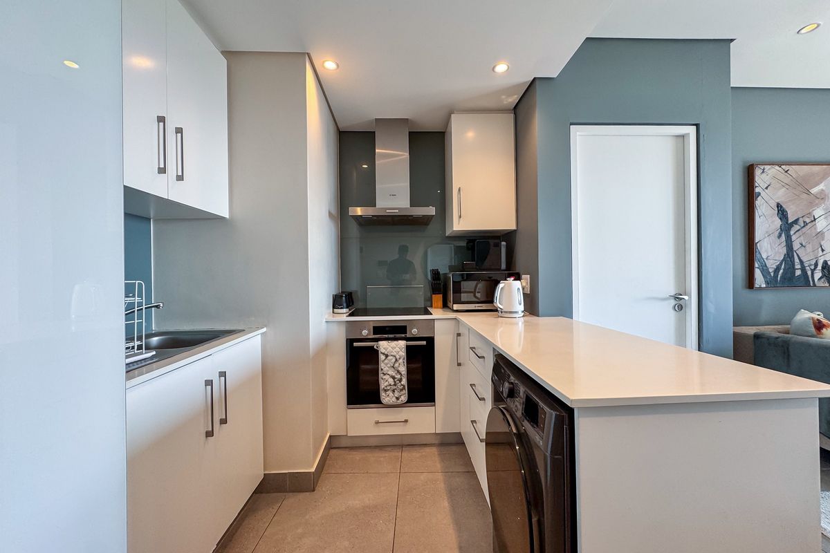 Modern kitchen featuring white cabinetry, stone countertops, integrated oven, hob, extractor fan, and a built-in washing machine.