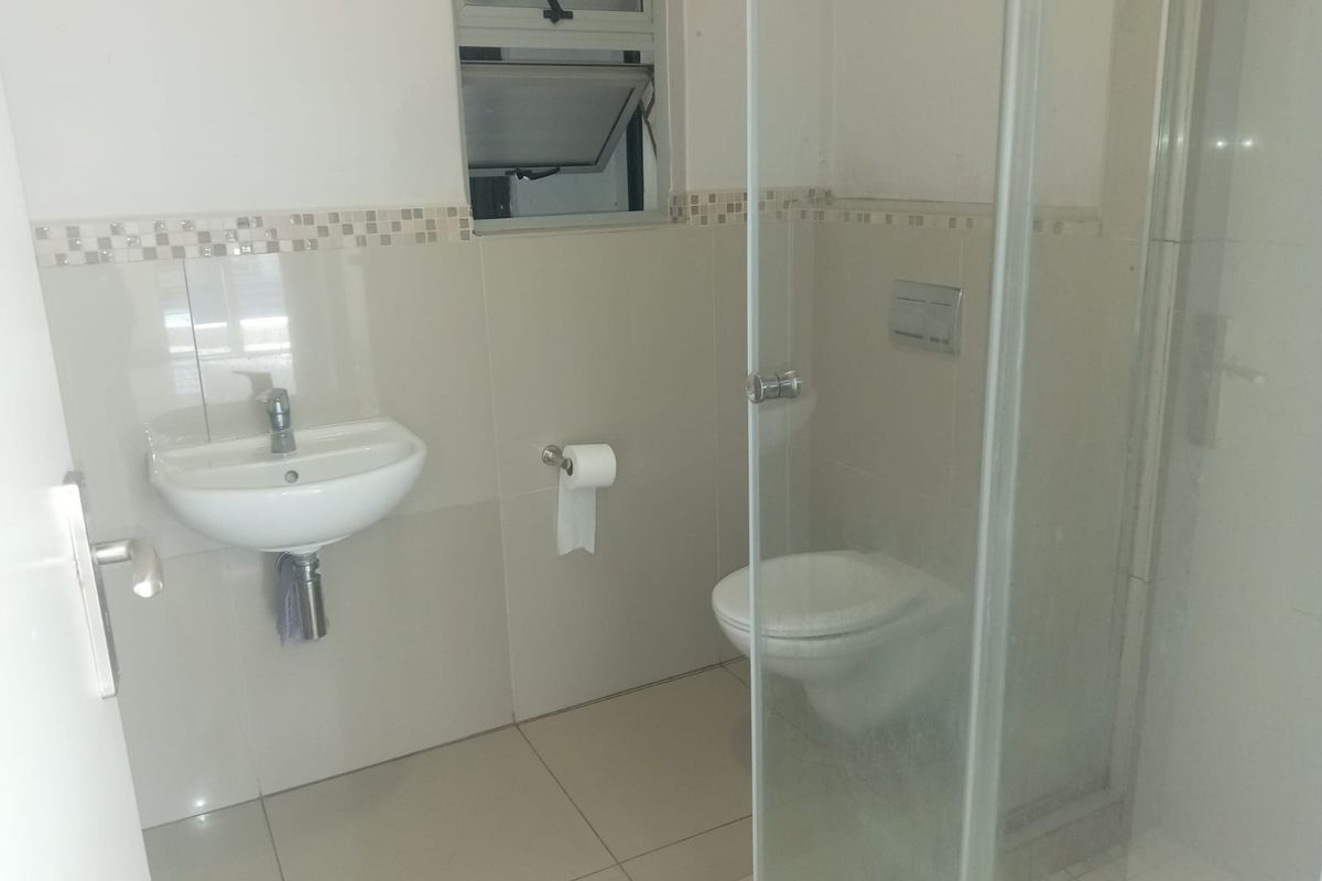 A compact bathroom featuring a wall-mounted basin, a wall-hung toilet, and a glass-enclosed shower with neutral wall and floor tiling.