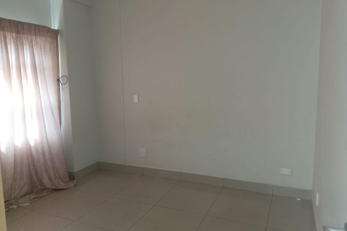 A bright, empty bedroom featuring neutral tiled flooring, plain walls, and a window with installed curtain tracks.