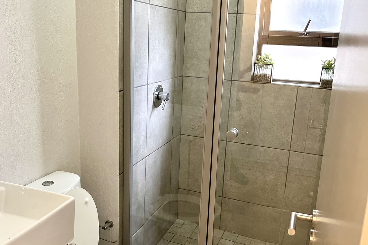 A compact bathroom featuring a glass-enclosed shower, a modern vanity basin, and a standard toilet with neutral wall and floor tiling.