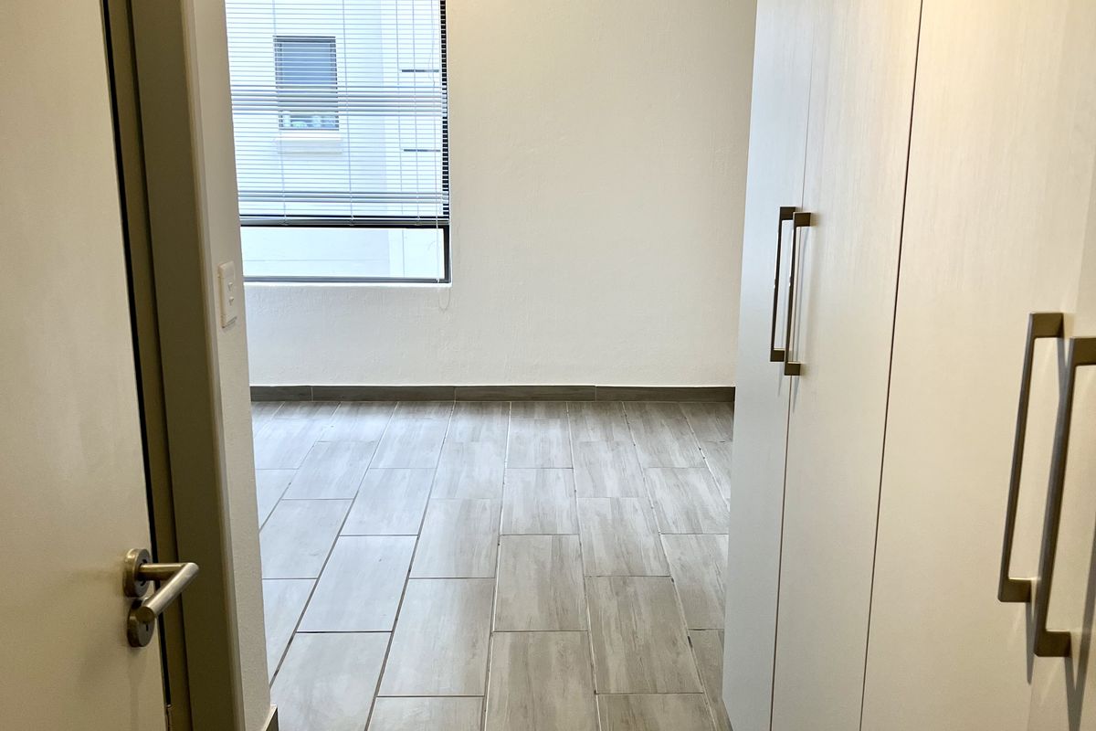 A bright, empty bedroom featuring modern wood-look tile flooring and built-in floor-to-ceiling cabinetry with sleek metal handles.