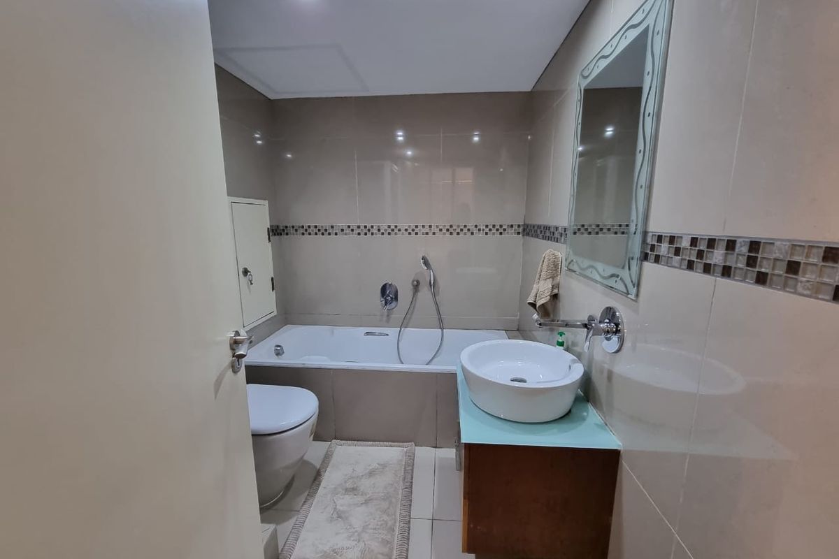 A modern bathroom featuring a built-in bathtub, a wall-mounted vanity with a vessel sink, and full-height wall tiling with decorative mosaic accents.