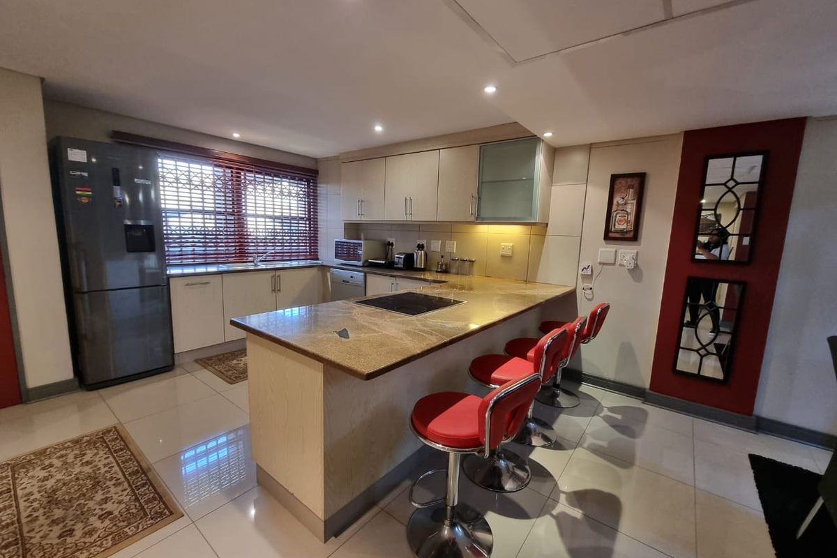 Modern kitchen featuring granite countertops, a breakfast bar, built-in cabinetry, and integrated cooktop, finished with polished floor tiles.