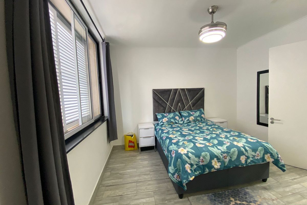 A well-lit bedroom featuring tiled flooring, a modern ceiling fan, and a large window with integrated blinds.