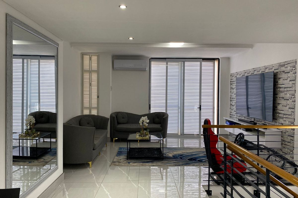 A bright and modern living room featuring polished floor tiles, recessed downlighting, a wall-mounted air conditioning unit, and a decorative stone-cladding feature wall.