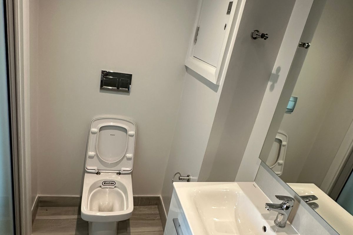 A modern bathroom featuring a wall-mounted toilet with a concealed cistern, a vanity basin with storage, and wood-look floor tiling.