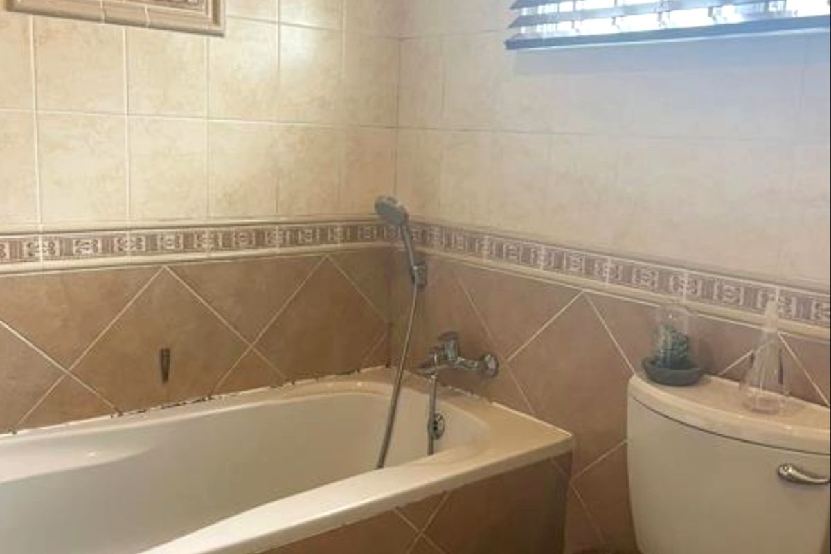 A functional bathroom featuring a built-in bathtub with shower mixer, ceramic wall tiling, and a standard toilet.