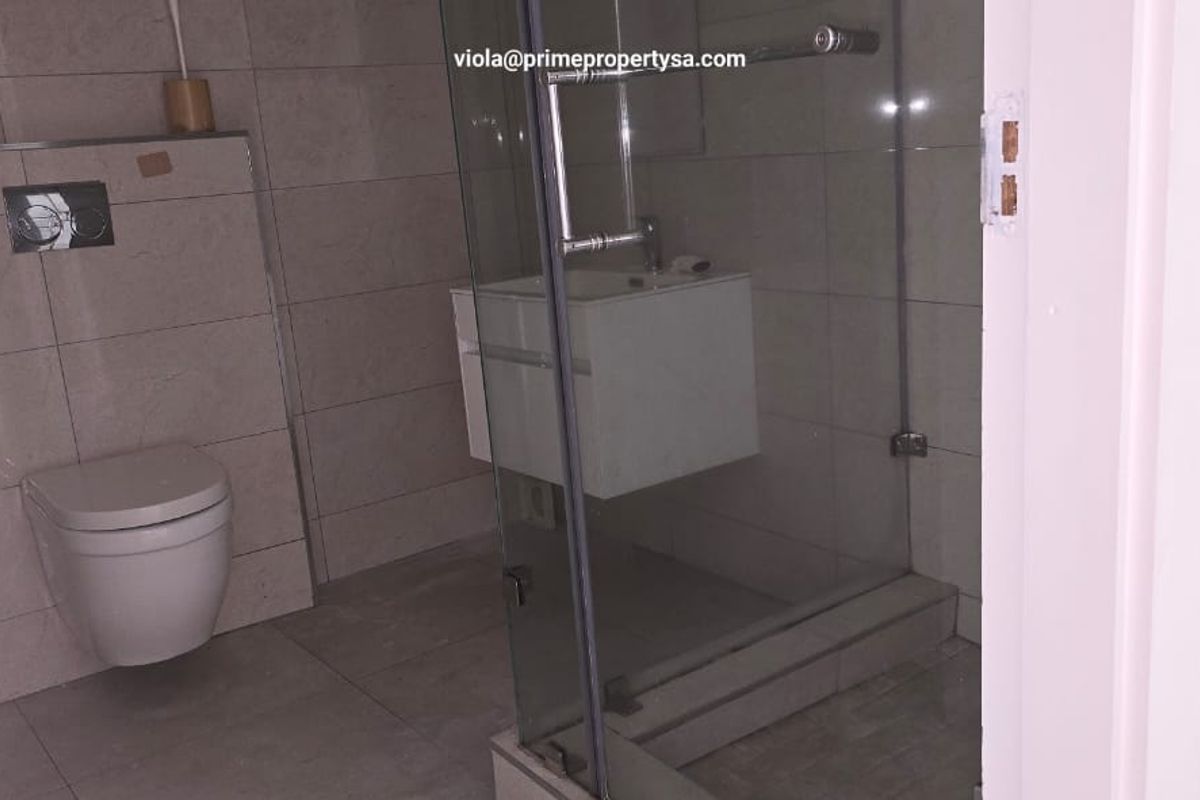 Modern bathroom featuring a wall-mounted toilet, glass-enclosed shower, and floating vanity with tiled walls and flooring.