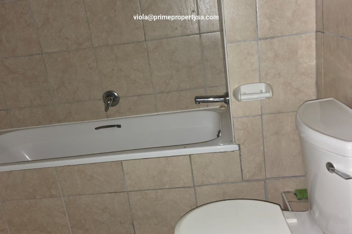 A functional bathroom featuring a built-in bathtub with chrome fixtures and a standard white toilet, finished with neutral wall tiling.