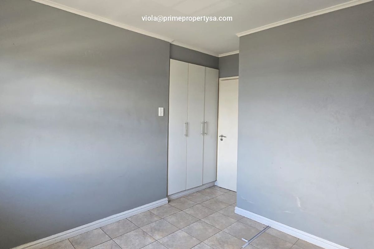 A neutral-toned bedroom featuring built-in cupboards, tiled flooring, and a standard interior door.