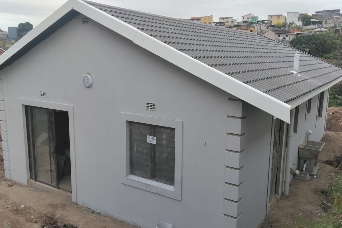 Rear view of a newly constructed house featuring a tiled roof, grey exterior walls, sliding door access, and an external utility sink.