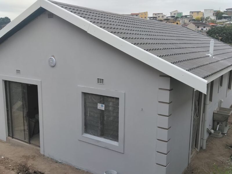 Rear view of a newly constructed house featuring a tiled roof, grey exterior walls, sliding door access, and an external utility sink.