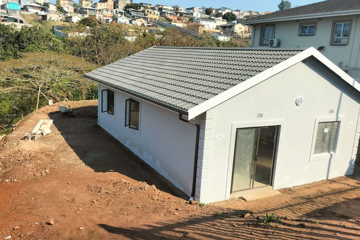 A newly constructed residential building featuring a tiled roof, plastered exterior walls, and sliding glass doors, set on an unfinished plot.