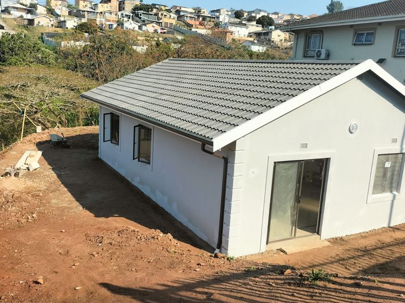 A newly constructed residential building featuring a tiled roof, plastered exterior walls, and sliding glass doors, set on an unfinished plot.