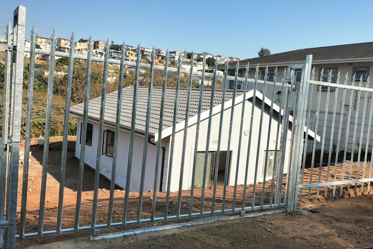Rear view of a residential house featuring a tiled roof, sliding glass door, and secure galvanized steel palisade fencing surrounding the unlandscaped yard.
