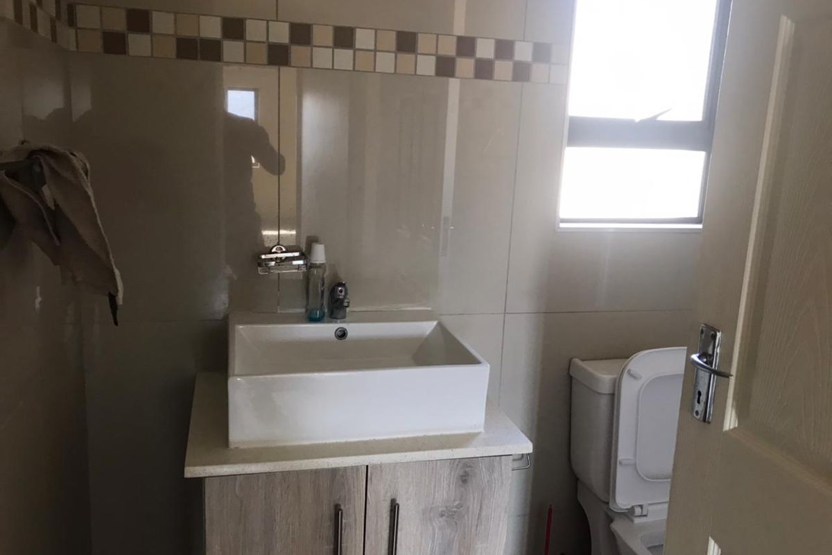 A compact bathroom featuring a modern vessel sink vanity, tiled walls with a decorative border, and a standard toilet.