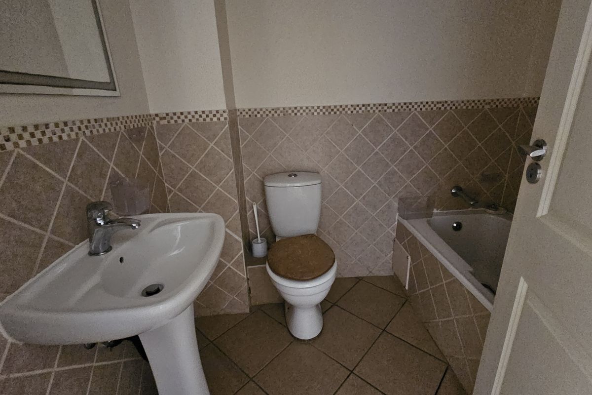 A functional bathroom featuring a pedestal basin, a standard toilet, and a built-in bathtub with tiled surround and decorative border.