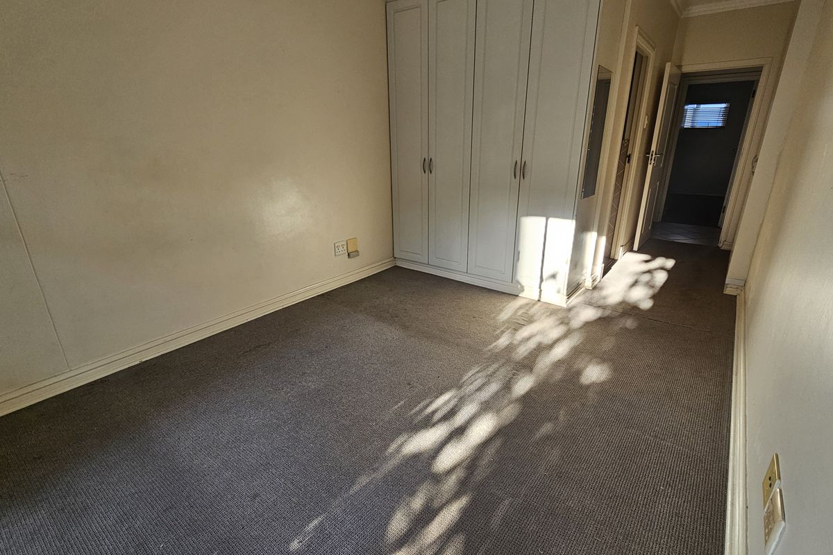 A bedroom featuring built-in cupboards and carpeted flooring, leading into a hallway.