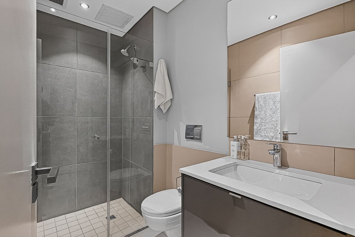 Modern bathroom featuring a glass-enclosed walk-in shower, wall-mounted toilet, and a sleek vanity with a basin and large mirror.