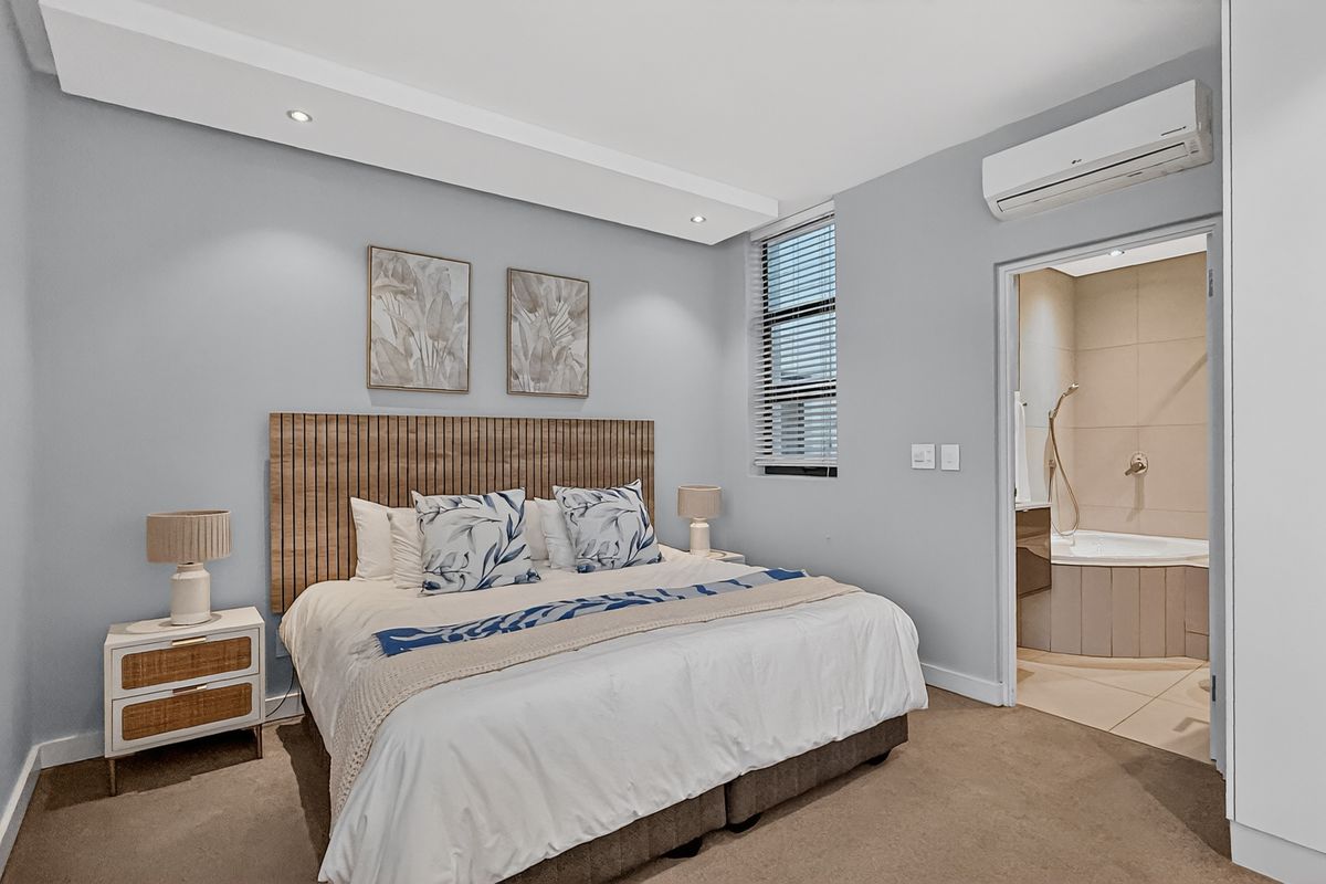 A well-maintained bedroom featuring a built-in air conditioning unit, recessed ceiling lighting, and an en-suite bathroom with a corner bathtub.