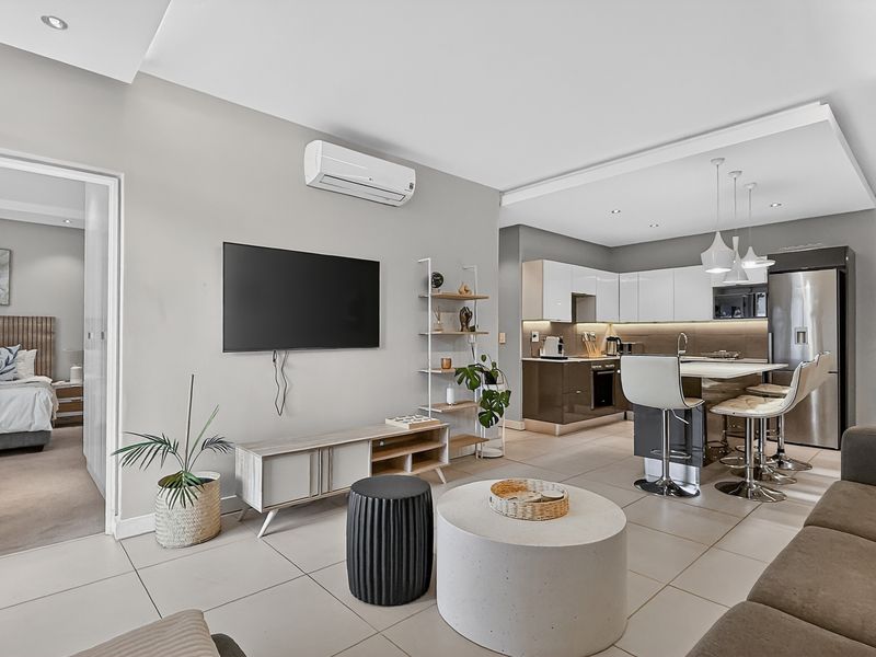 Modern open-plan living area featuring a sleek kitchen with high-gloss cabinetry, breakfast island, and integrated appliances, seamlessly flowing into the lounge space.