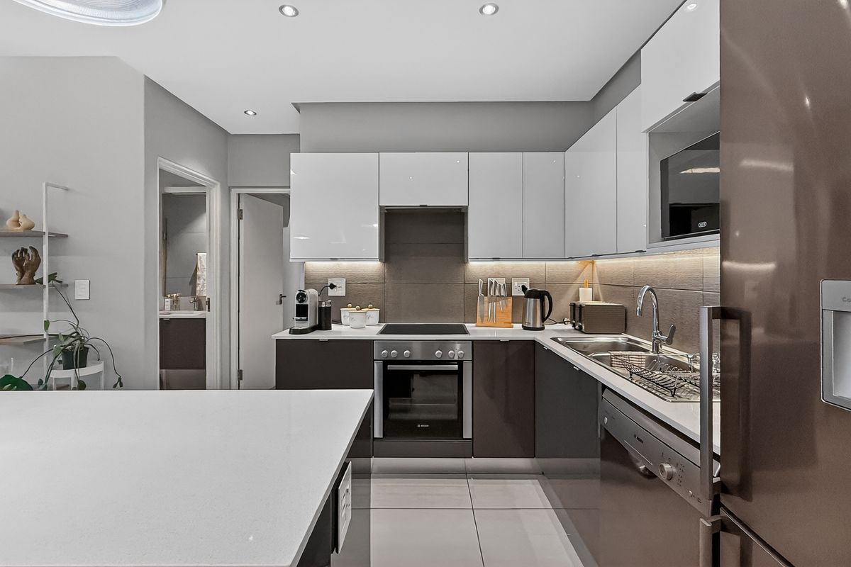 Modern kitchen featuring sleek high-gloss cabinetry, stone countertops, integrated oven, hob, and extractor fan with recessed ceiling lighting.