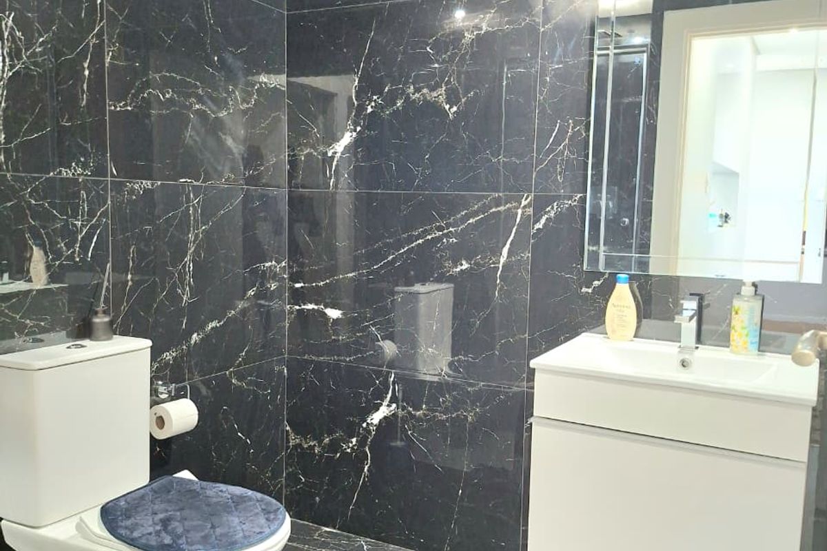 Modern bathroom featuring dark marble-effect wall and floor tiling, a wall-mounted vanity with integrated basin, and a contemporary toilet suite.