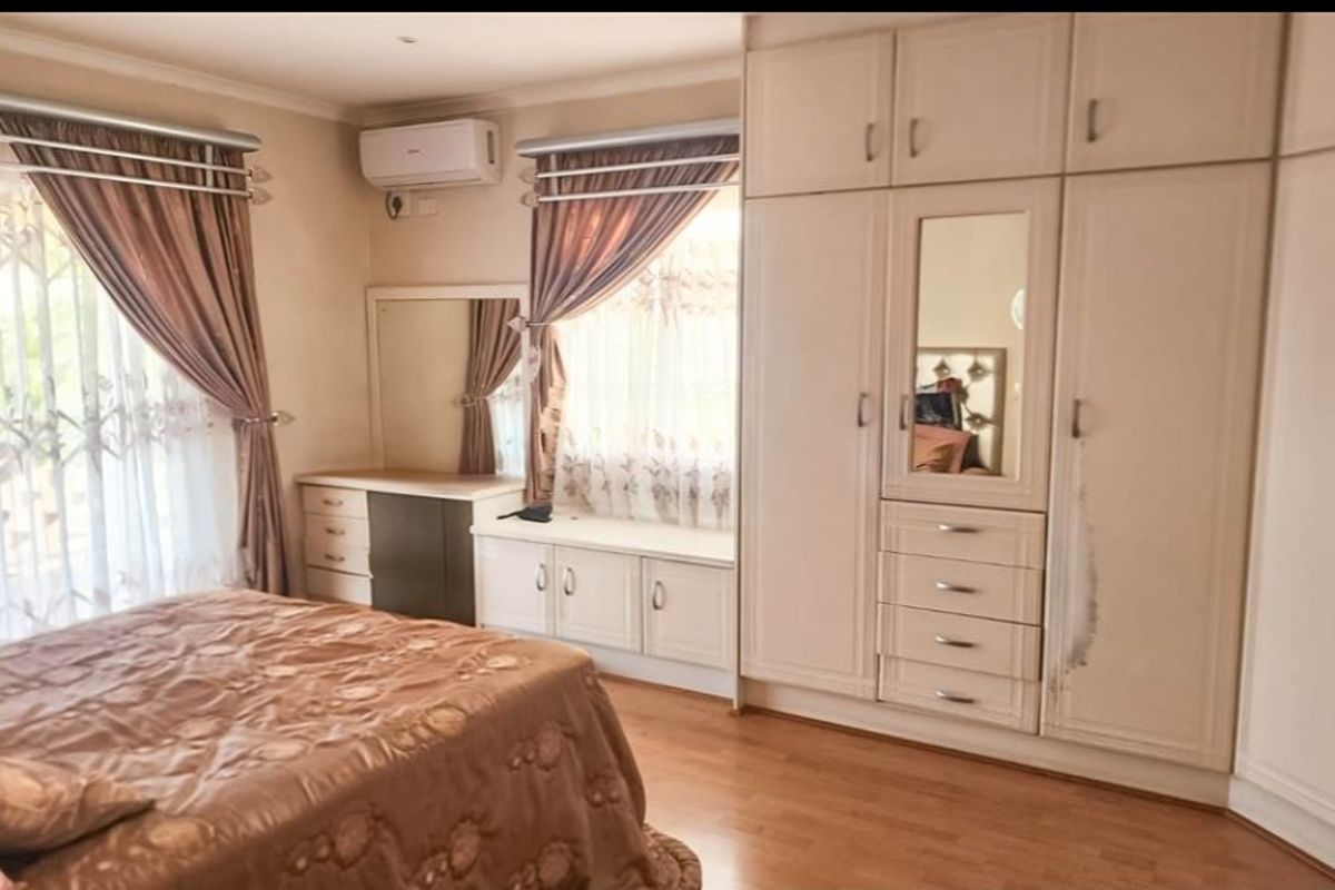 Spacious bedroom featuring extensive built-in cabinetry, integrated vanity unit, laminate flooring, and a wall-mounted air conditioning unit.