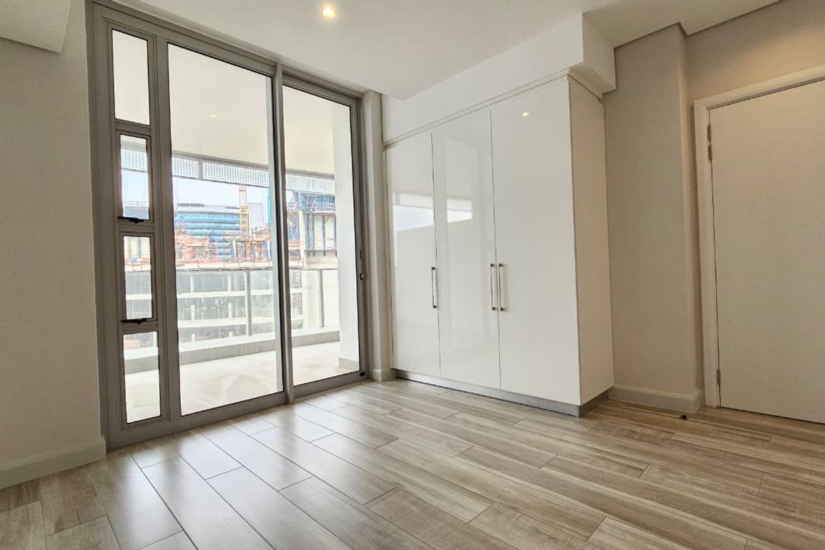 Modern bedroom featuring light wood-look tile flooring, built-in high-gloss white cabinetry, and large sliding glass doors providing access to a private balcony.