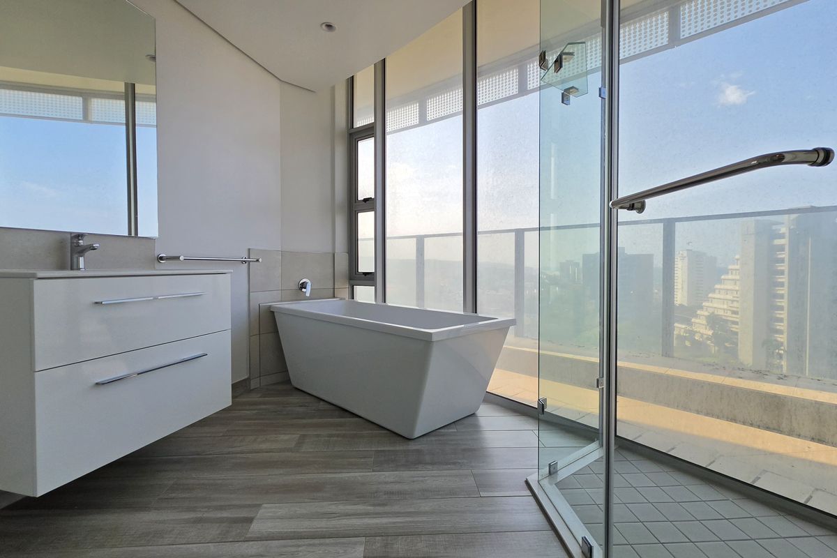 Modern bathroom featuring a freestanding bathtub, wall-mounted vanity, glass-enclosed shower, and floor-to-ceiling windows with expansive city views.