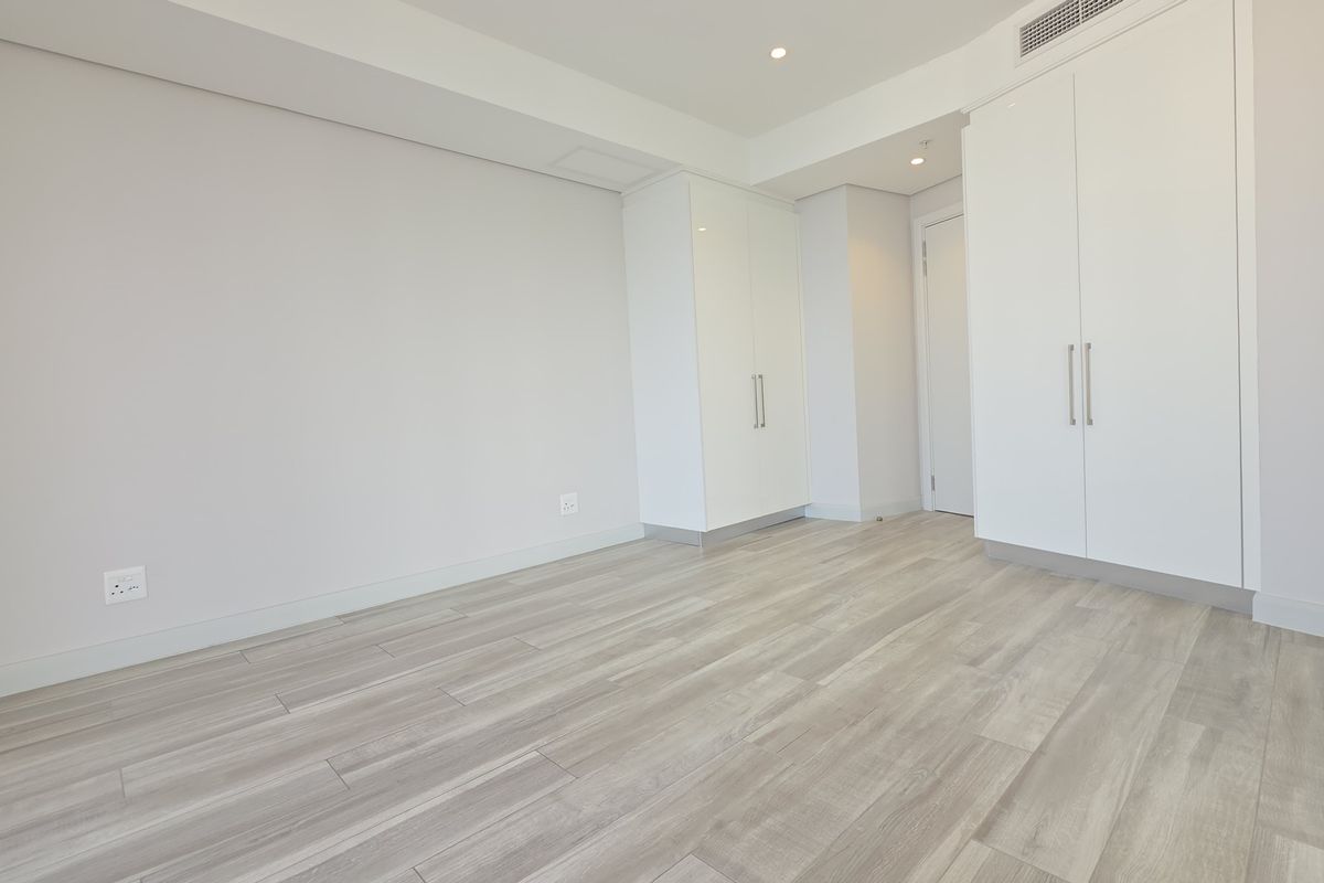 A bright, modern bedroom featuring light wood-look flooring, built-in white cabinetry, and integrated ceiling air conditioning vents.