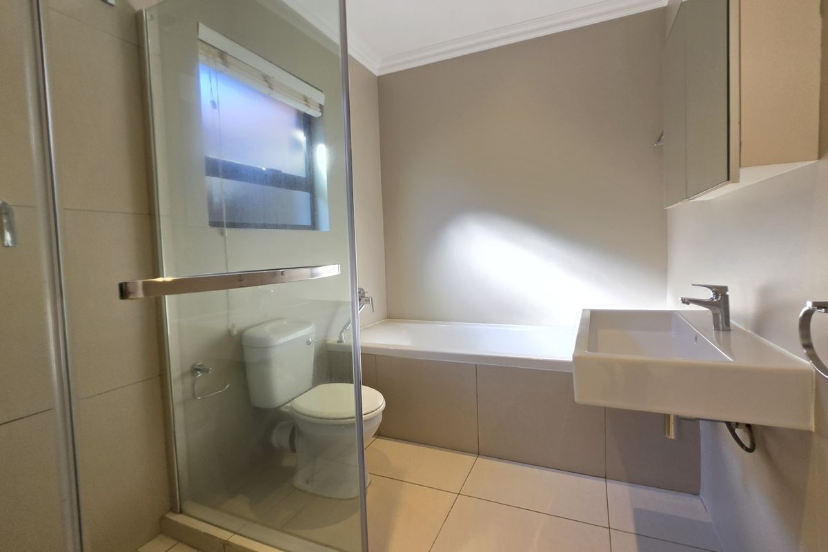 A modern bathroom featuring a glass-enclosed shower, a built-in bathtub, a wall-mounted basin, and a toilet with neutral floor and wall tiling.