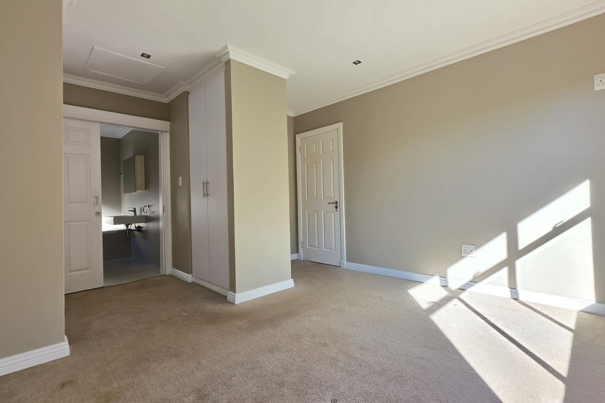 A bright, carpeted bedroom featuring built-in cupboards, crown molding, and an en-suite bathroom access.