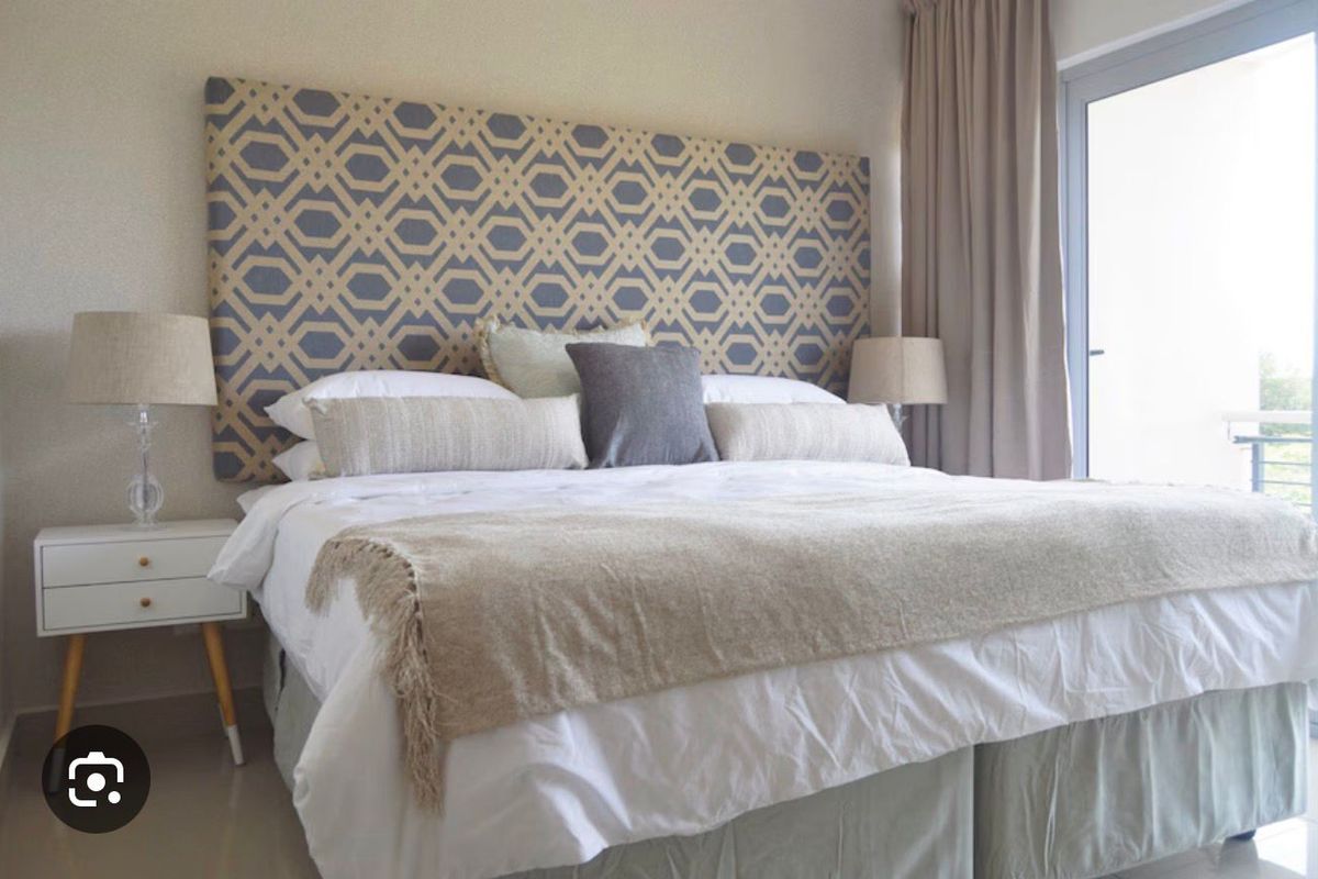 A well-lit bedroom featuring a large patterned headboard and direct access to an outdoor balcony through a glass door.