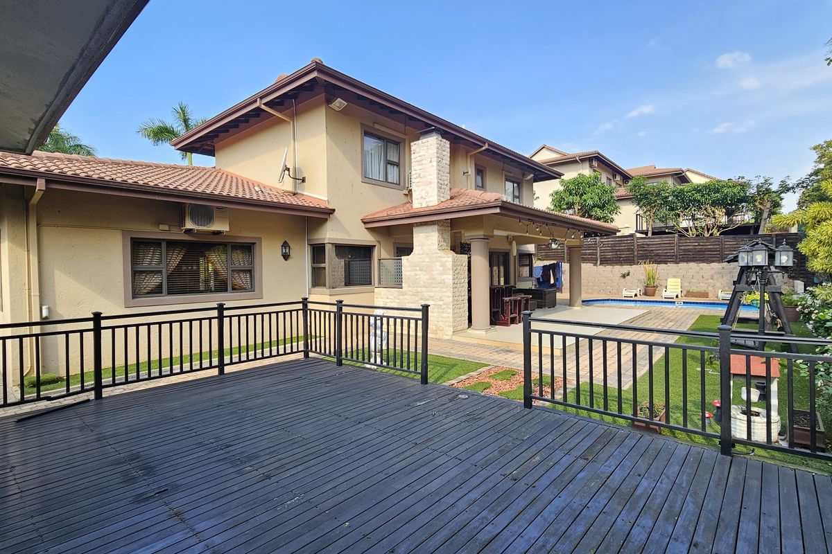 Spacious rear exterior featuring a raised timber deck, paved patio area, stone-clad chimney, and a private swimming pool set within a landscaped garden.