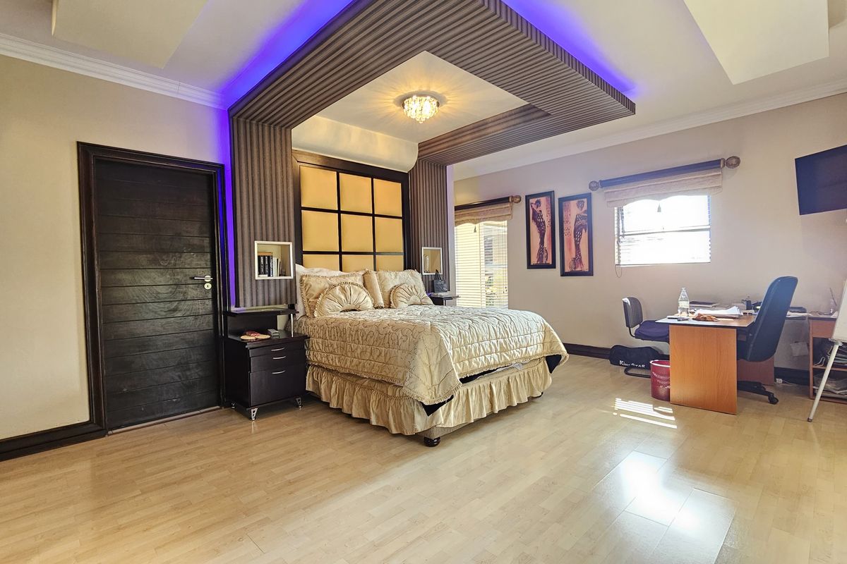 Spacious bedroom featuring a custom bulkhead ceiling with integrated LED lighting, wood-look laminate flooring, and a dark timber door.
