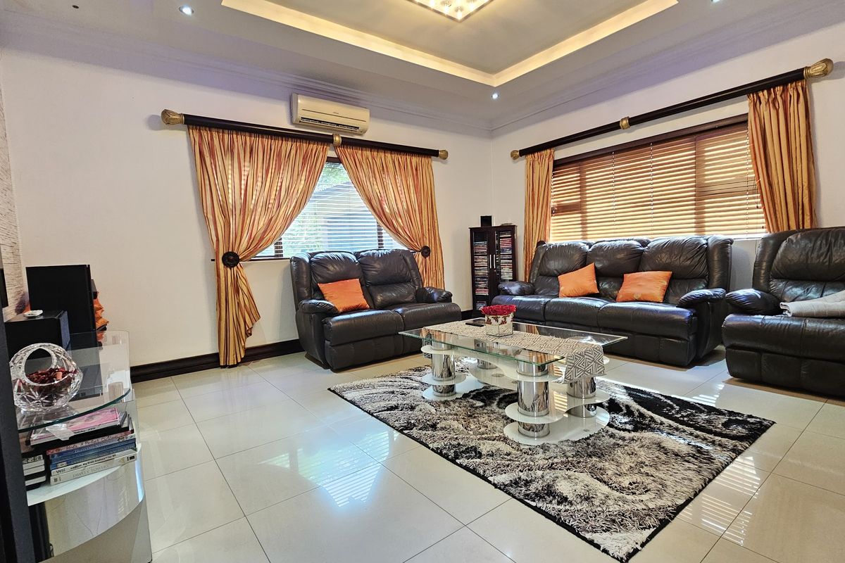 Spacious living room featuring polished floor tiles, recessed tray ceiling with downlighting, and a wall-mounted air conditioning unit.
