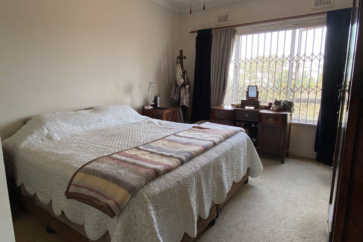 A bedroom featuring neutral walls, carpeted flooring, and a large window fitted with a security gate and curtain rods.