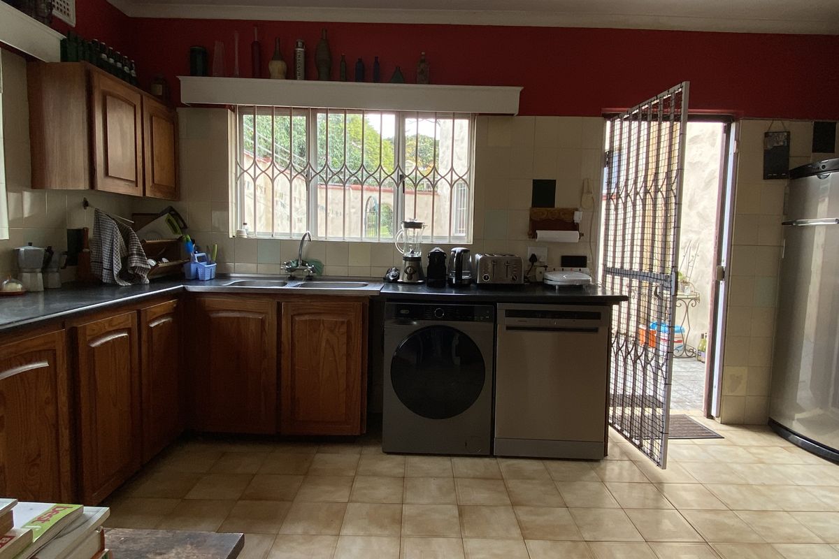 A functional kitchen featuring wooden cabinetry, tiled countertops, and direct access to an outdoor area through a security gate.