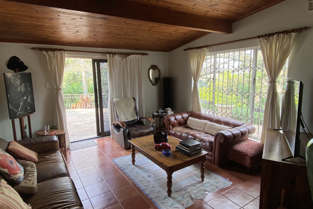 A living room featuring terracotta floor tiles, a vaulted timber-paneled ceiling, and large windows with security bars, providing access to an outdoor patio area.