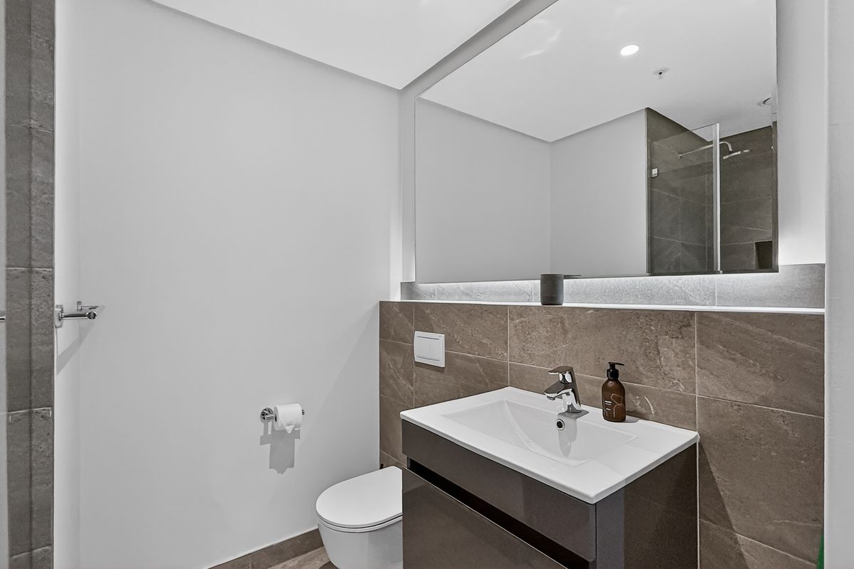 Modern bathroom featuring a sleek vanity with integrated basin, large wall-mounted mirror with LED lighting, and contemporary tiled finishes.