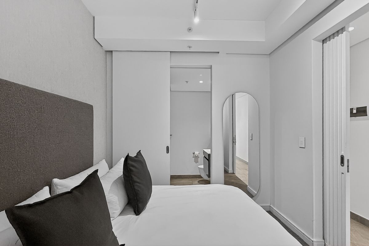 Modern bedroom featuring a neutral color palette, integrated sliding door access to an en-suite bathroom, and clean architectural lines.