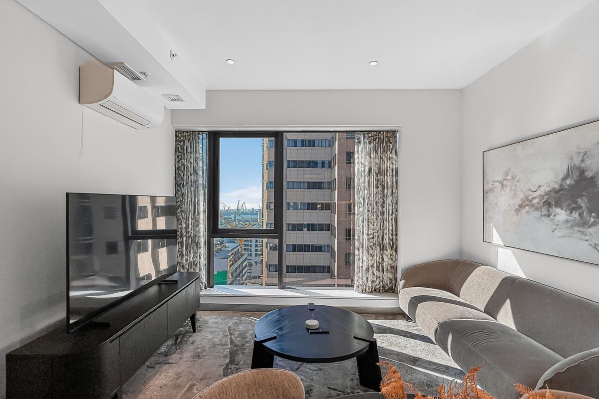 A bright and modern living room featuring a wall-mounted air conditioning unit, large window with city views, and recessed ceiling lighting.